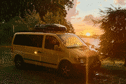 Pixelated photo of a yellow campervan by a lake at sunset