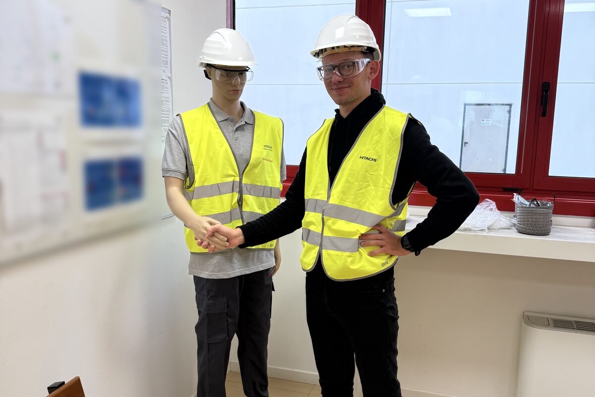 Piotr in a hard hat and high-visibility vest shaking hands with a safety training mannequin