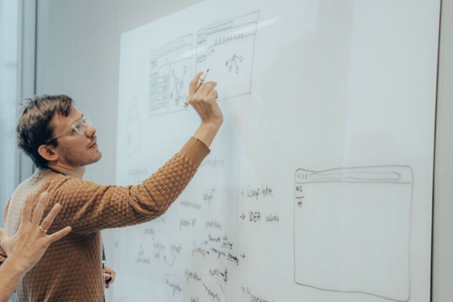 Piotr sketching a screen layout on a whiteboard during a team workshop